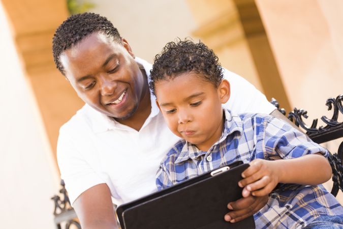 Black Father and Son Using Tablet On Balcony