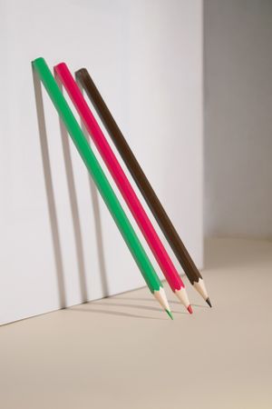 Three pencils standing against a beige wall