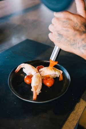 Tattooed chef hands blow torching prawn