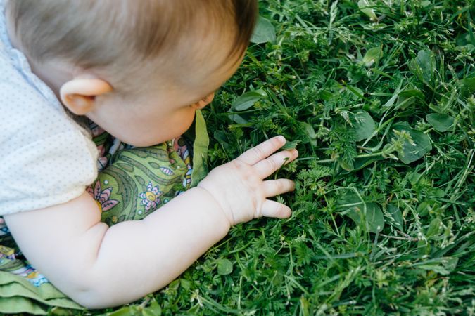 Baby on cloth diaper on lawn exploring grass