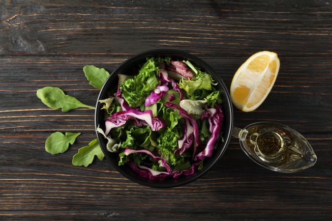 Black bowl with salad and ingredients on wooden background, top view