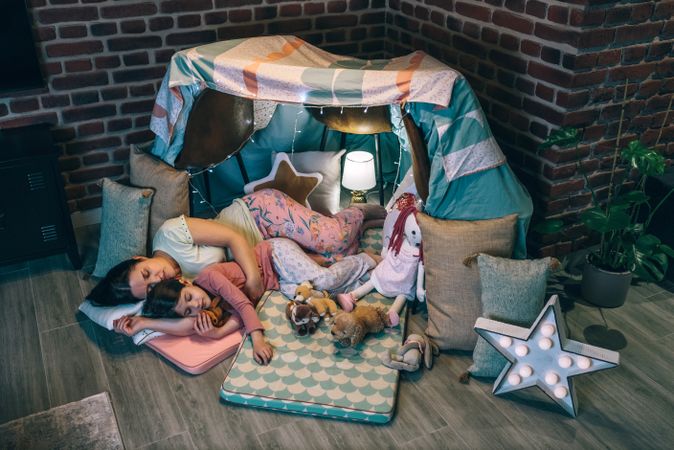 Loving mother and daughter sleeping together lying over mats in cosy diy tent. Serene atmosphere.
