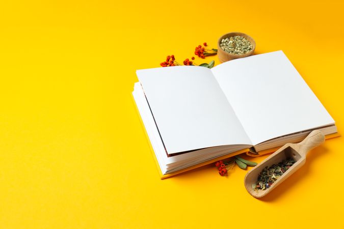 Alternative medicine: blank book and ingredients on yellow background