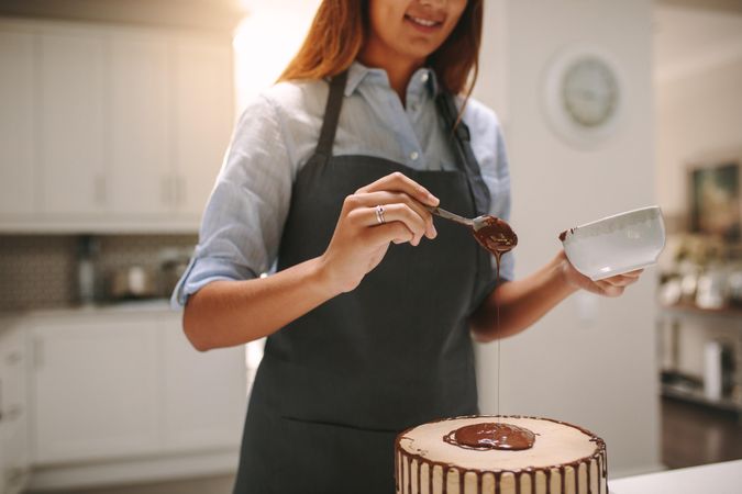Woman pouring liquid chocolate on cake for decoration