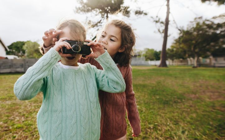 Two little girls taking photographs using camera at the playground