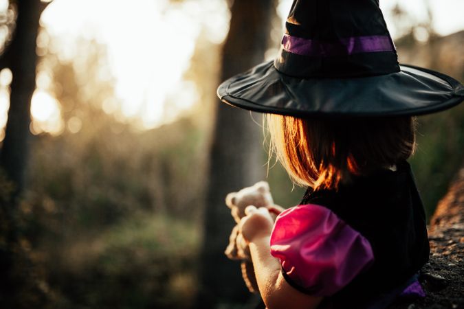 Back of girl holding her teddy bear in witch costume