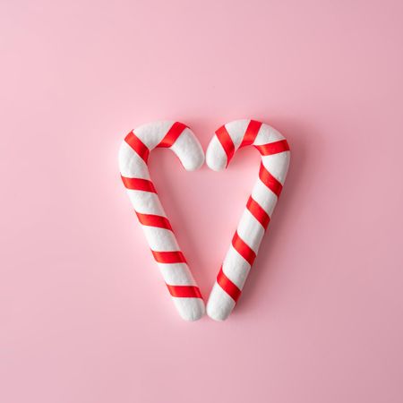 Candy canes in heart shape on pink background