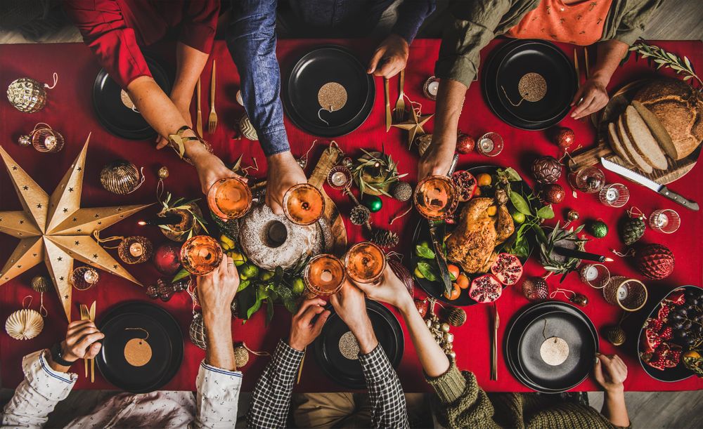 Group of people toasting with drinks at festive red table with cake, roast chicken, and decorations