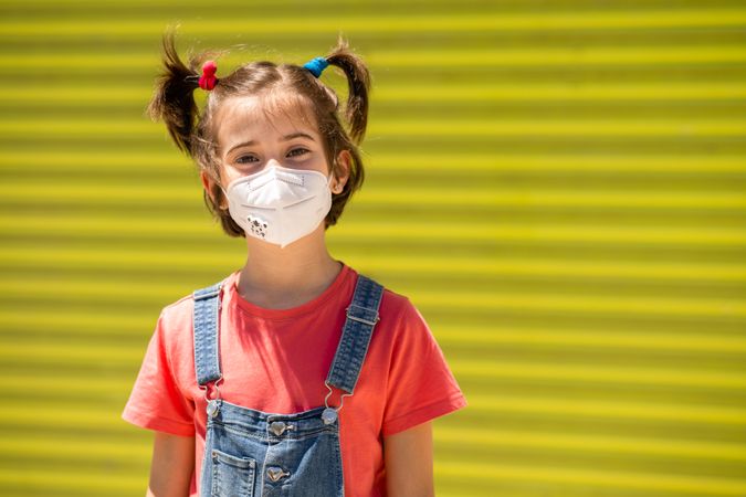 Cute child in protective mask against a yellow wall