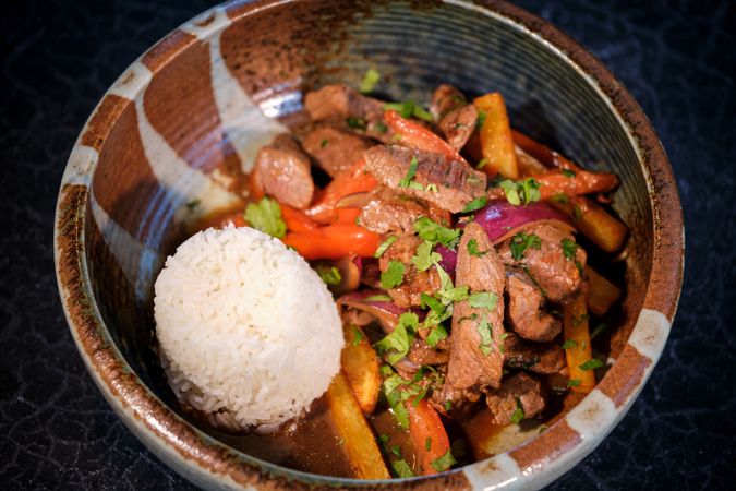 Bowl with delicious fried beef with vegetables and rice on black table