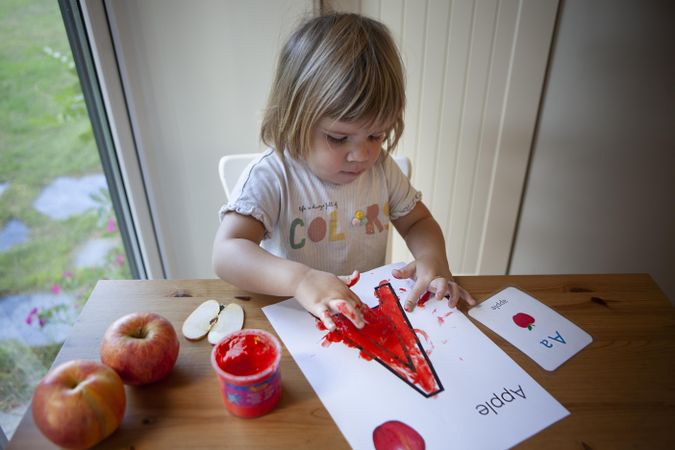 Girl in coloring letter A with red on kitchen table