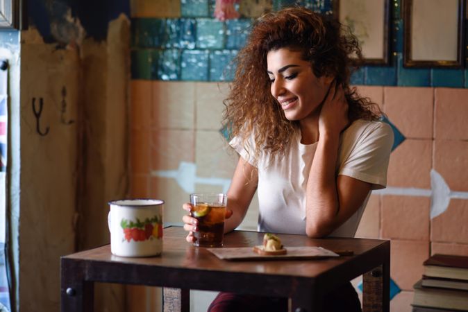 Arab woman in casual clothes smiling and looking down in the distance with soda at restaurant table