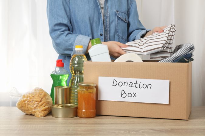 Woman puts clothes in donation box on wooden table