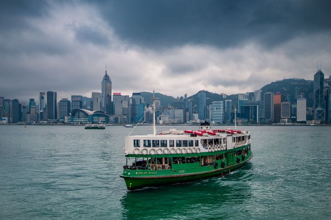 Green boat on water near city buildings in Hong Kong