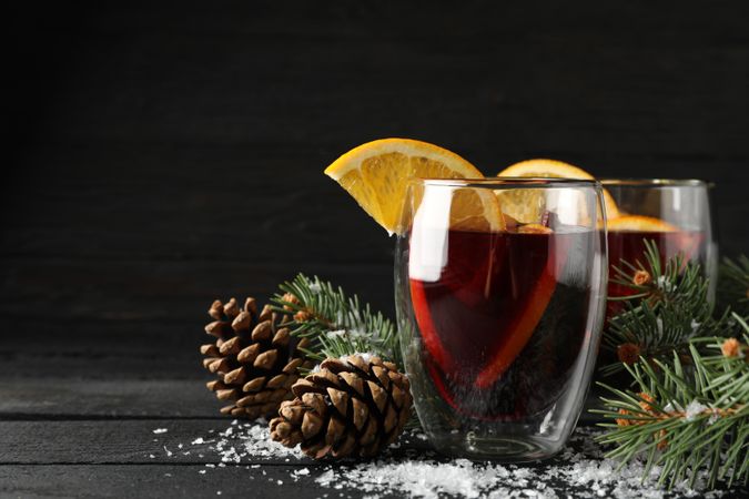 Glasses of tasty mulled with orange on decorated background, space for text