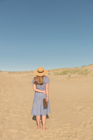 adult woman standing with book on sand dune on hot summer day