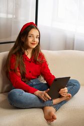 Portrait of smiling teen girl holding tablet on sofa.
