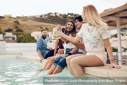 Friends partying outdoor sitting by the pool and toasting drinks 0K6Ozb