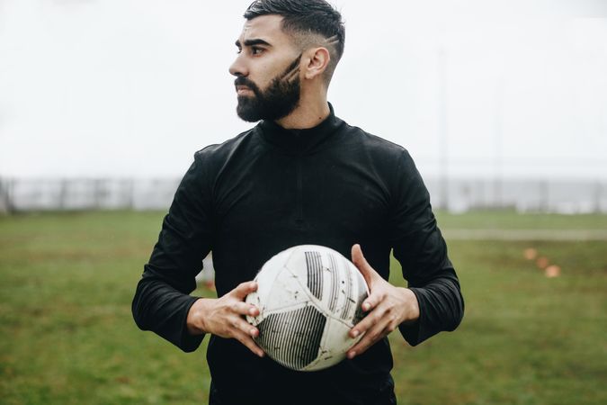 Portrait of a football player standing on field holding a ball looking away