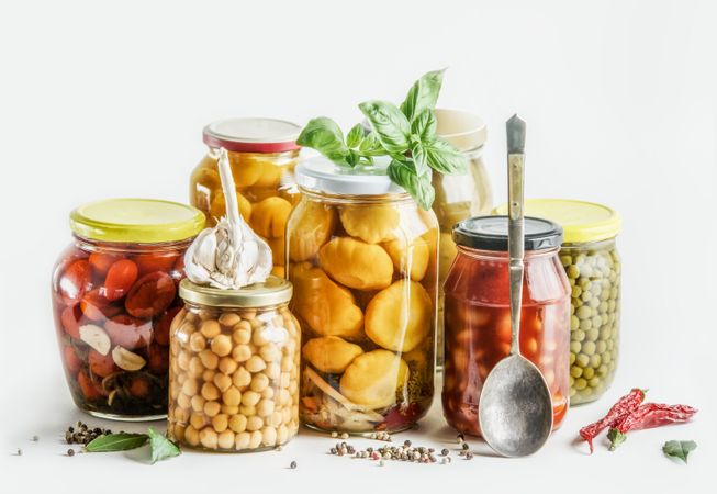Preserved vegetables selection in glass jars with herbs, spices and spoon