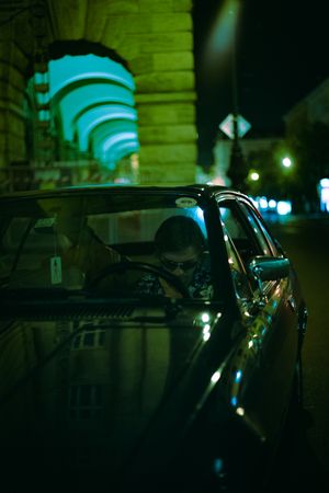 Young man with sunglasses sitting on driver seat of an old car at night