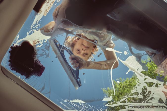 Cute boy using glass washing tool and cleaning car window
