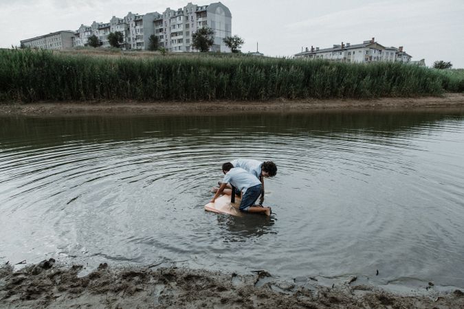 Kid brothers playing in dirty pond in daylight