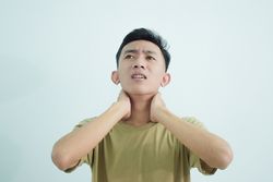 Asian young man touching neck in pain and wincing