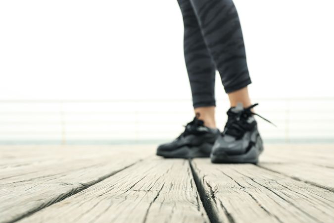 Female legs in leggings and sneakers on wooden floor at sea