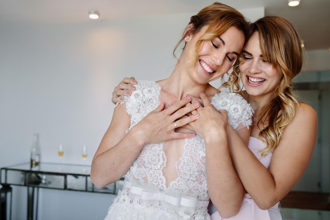 Smiling bridesmaid giving a tender hug to beautiful bride on her wedding day