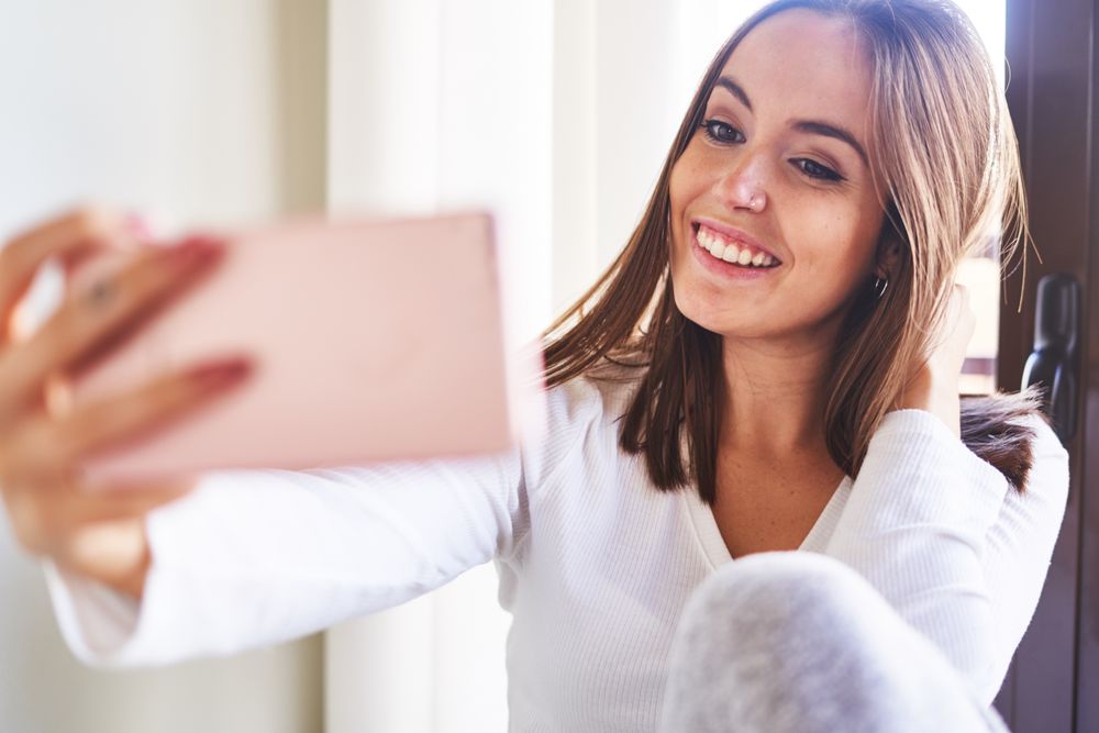 Woman showing tongue and taking selfie on smartphone