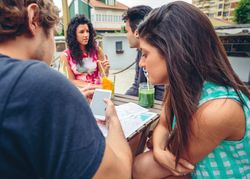 Male showing female friend something on phone at table outdoors