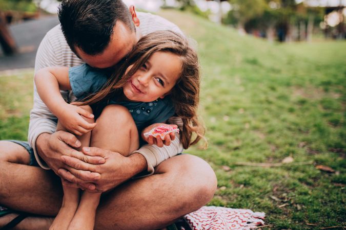 Father holds daughter in his lap in the park