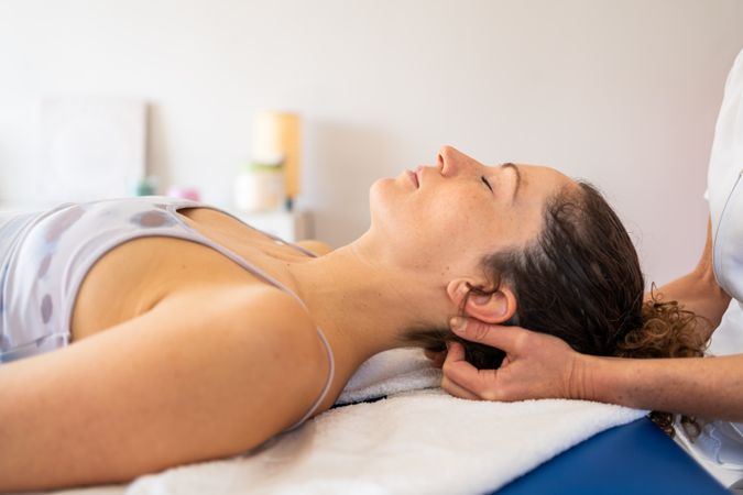Unrecognizable osteopath working on neck of client during rehabilitation in clinic