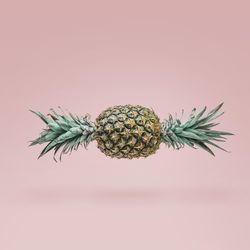 Pineapple in shape of candy with green top on both ends on blush background