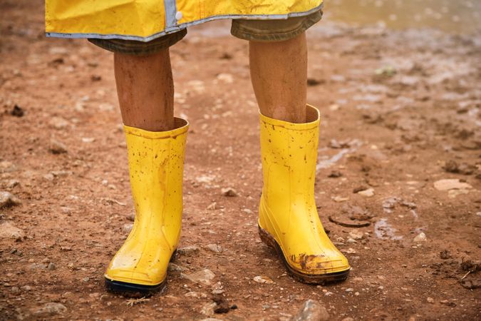 Crop child wearing yellow raincoat and standing in mud