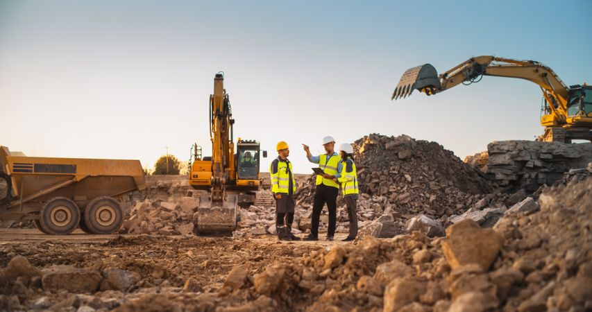 Construction Site With Excavators on Sunny Day: Diverse Team Of Male And Female Real Estate Developers Discussing Project. Engineer, Architect, Investor Talking About Apartment Building, Using Tablet
