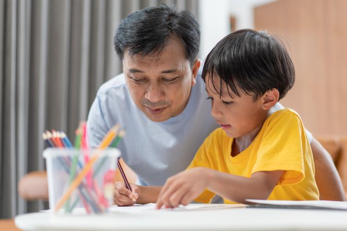 Asian father helping son to do homework at home