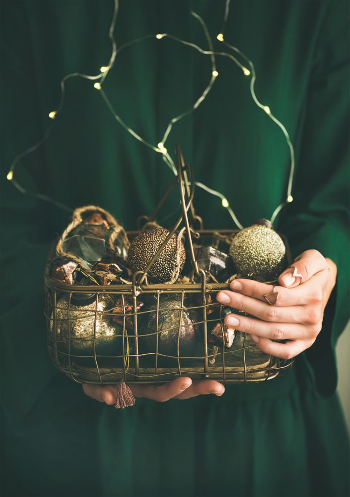 Woman in green dress holding wire basket of gold holiday decorations
