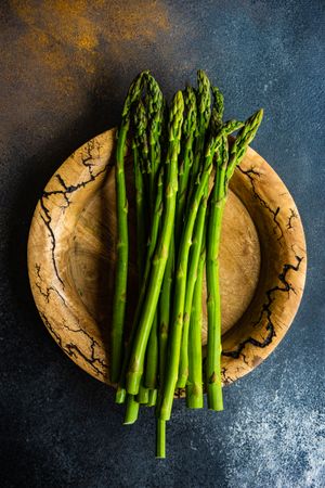 Loose raw asparagus on brown plate on dark counter