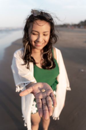 A young Hispanic woman is showing a seashell at the beach during sunset