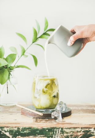 Iced matcha drink with hand pouring cream from grey pitcher