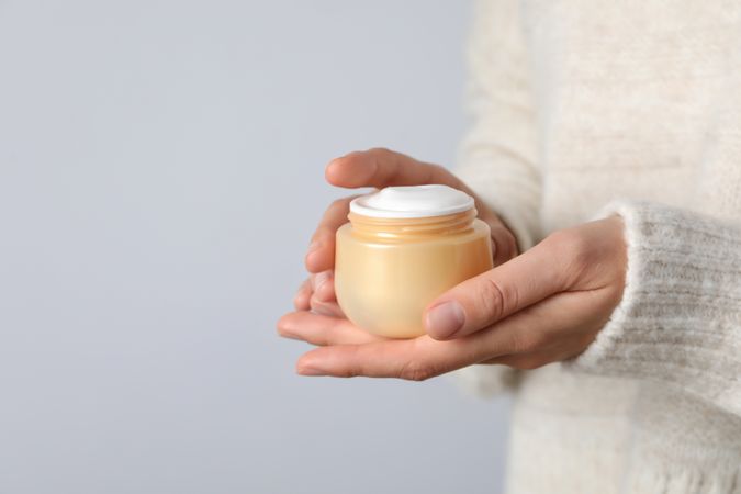 A jar of hand cream in hands on a light background.