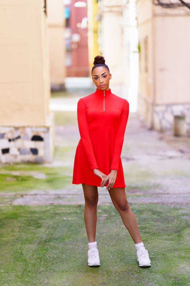 Serious woman in casual red dress standing in alley on sunny day