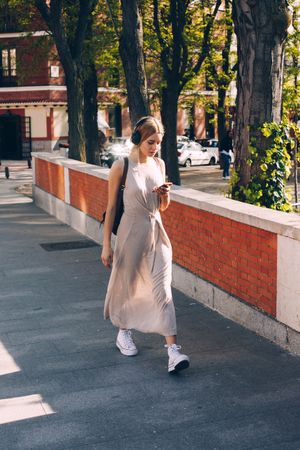 Young woman with headphones and smartphone walking outdoors