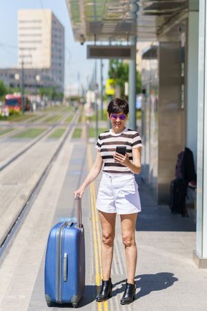 Woman standing with large suitcase at train station