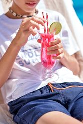 Crop boy holding cocktail and relaxing on sunbed at poolside
