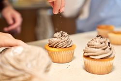 Crop woman decorating cupcakes with chocolate