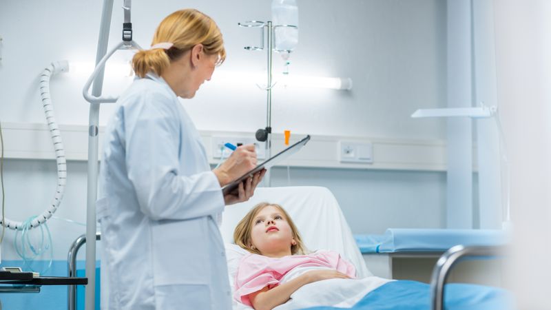 Recovering Little Girl Lies on a Bed In the Hospital, Friendly Doctor With Clipboard Asks Questions