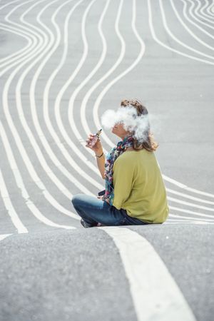 Modern relaxed woman vaping while sitting on marked road